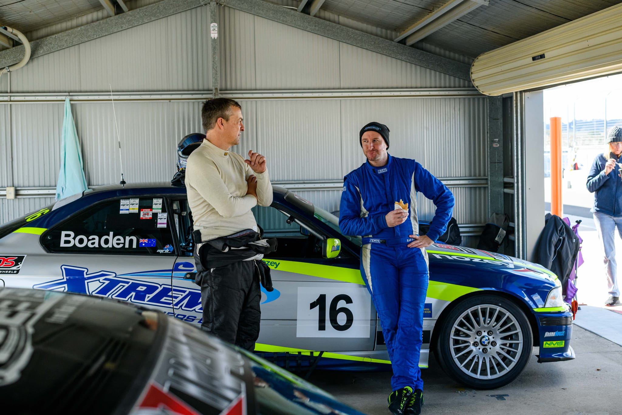 Two drivers chatting in the garage beside the blue and silver #16 Boaden BMW at Wakefield Park during MRA Round 6